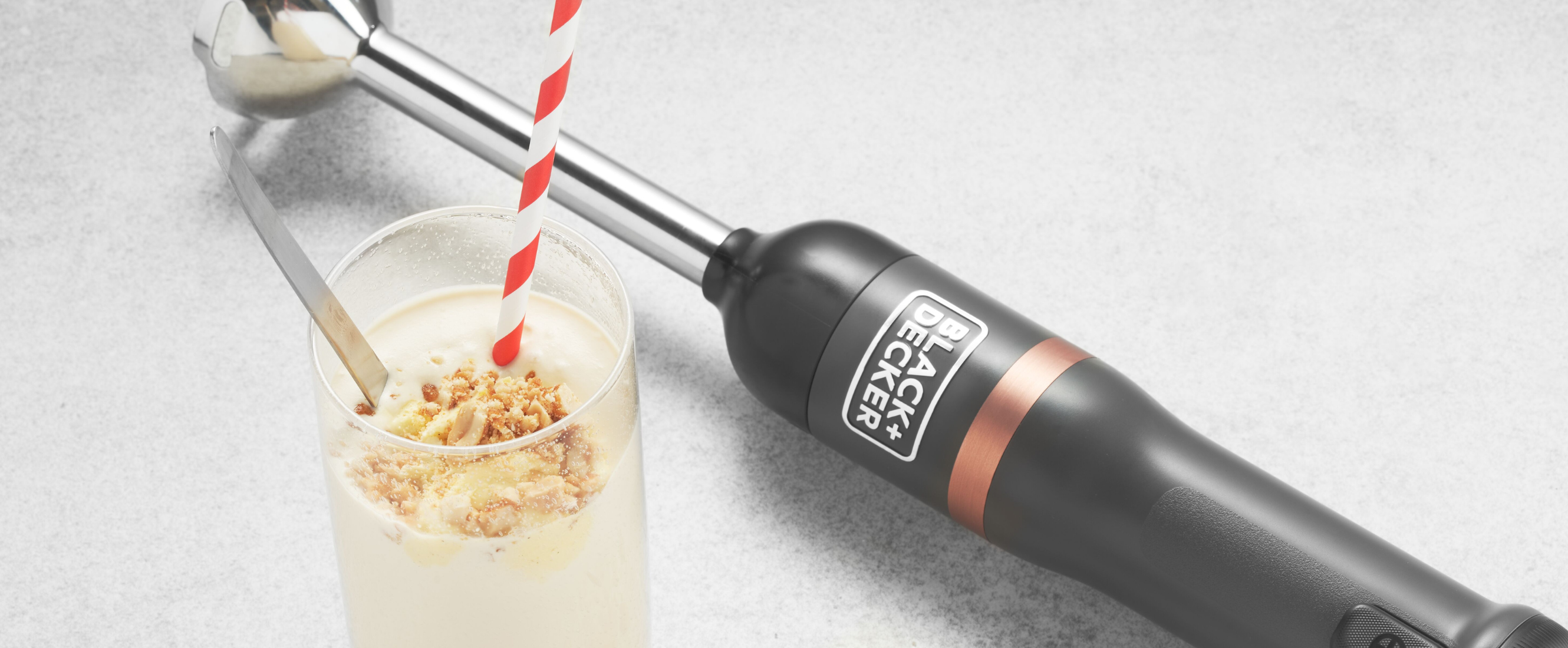 Grey, Black-and-decker kitchen wand with immersion blender attachment lying next to a vanilla malted milkshake in a glass cup