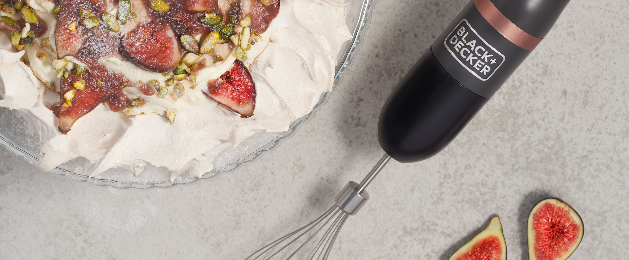 Grey, Black-and-decker kitchen wand with whisk attachment lying next to a pavlova with roasted figs