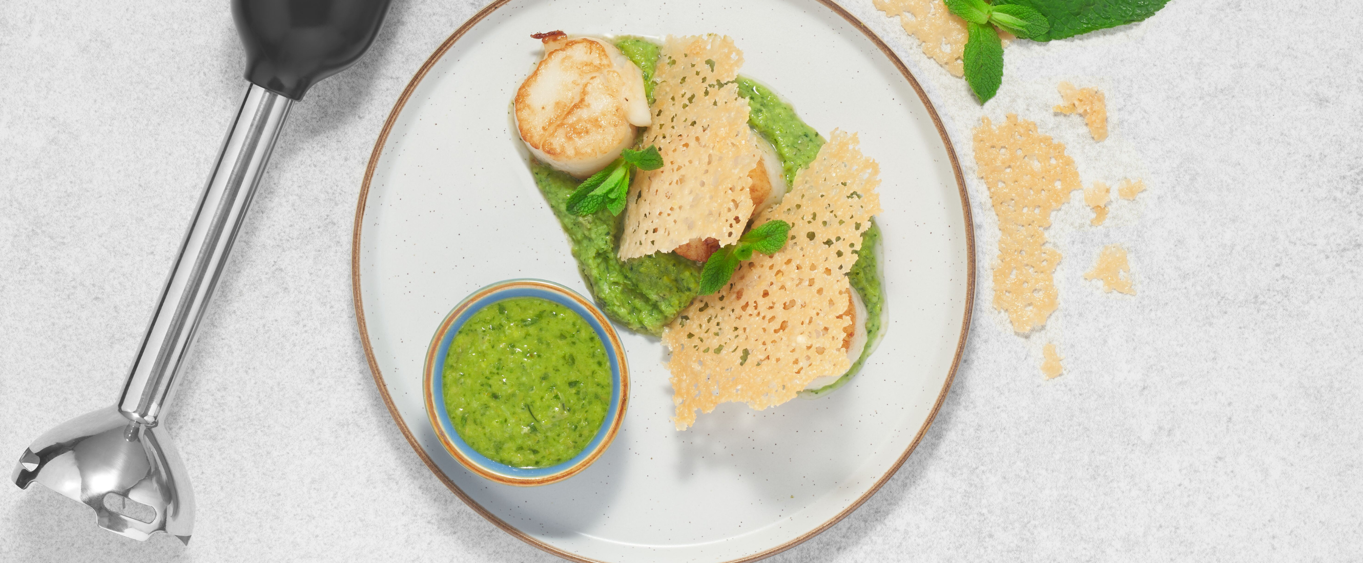 Grey, Black-and-decker kitchen wand with immersion blender attachment lying next to a plate of scallops on pea puree