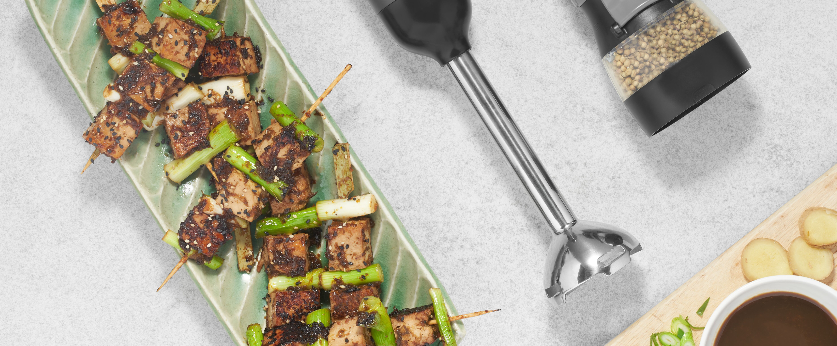 Grey, Black-and-decker kitchen wand with immersion blender and spice grinder attachments lying next yakitori tofu and toppings
