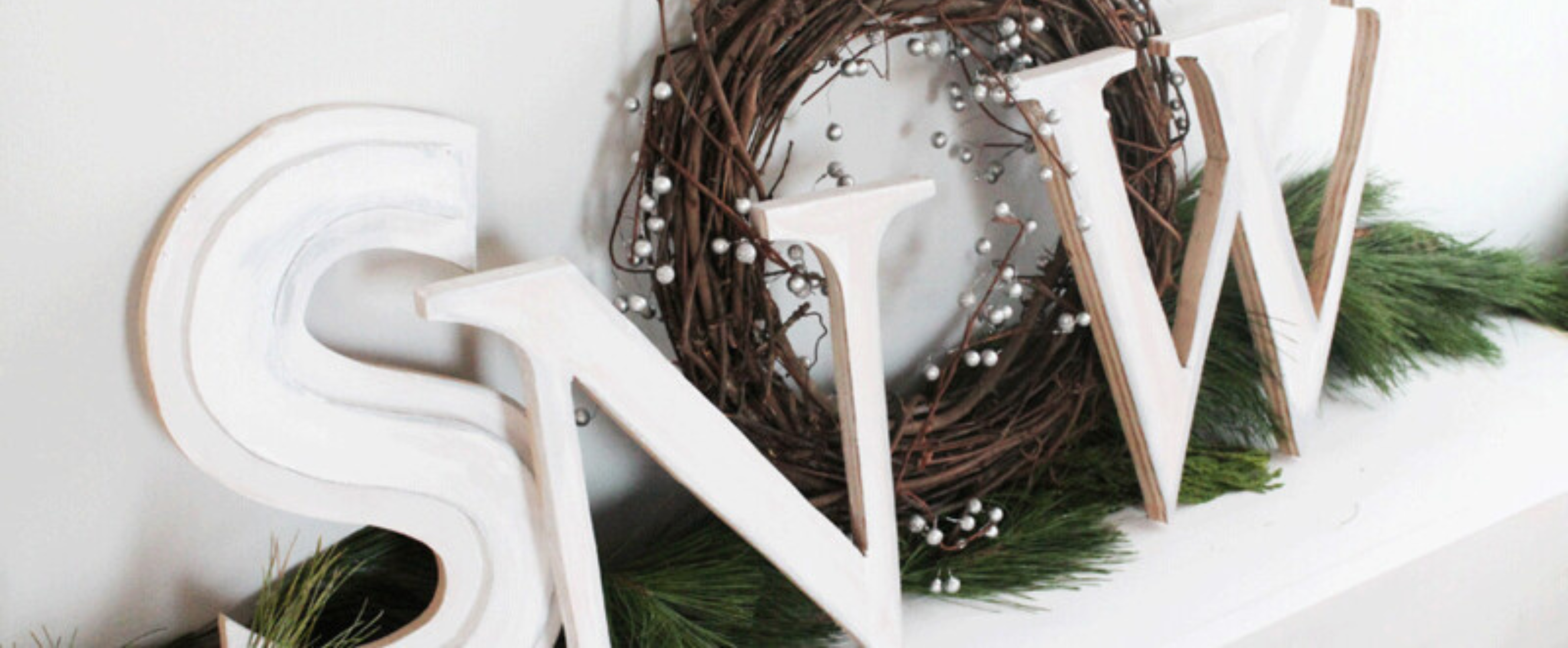 "Snow" sign with garland and wreath sitting on fireplace mantle