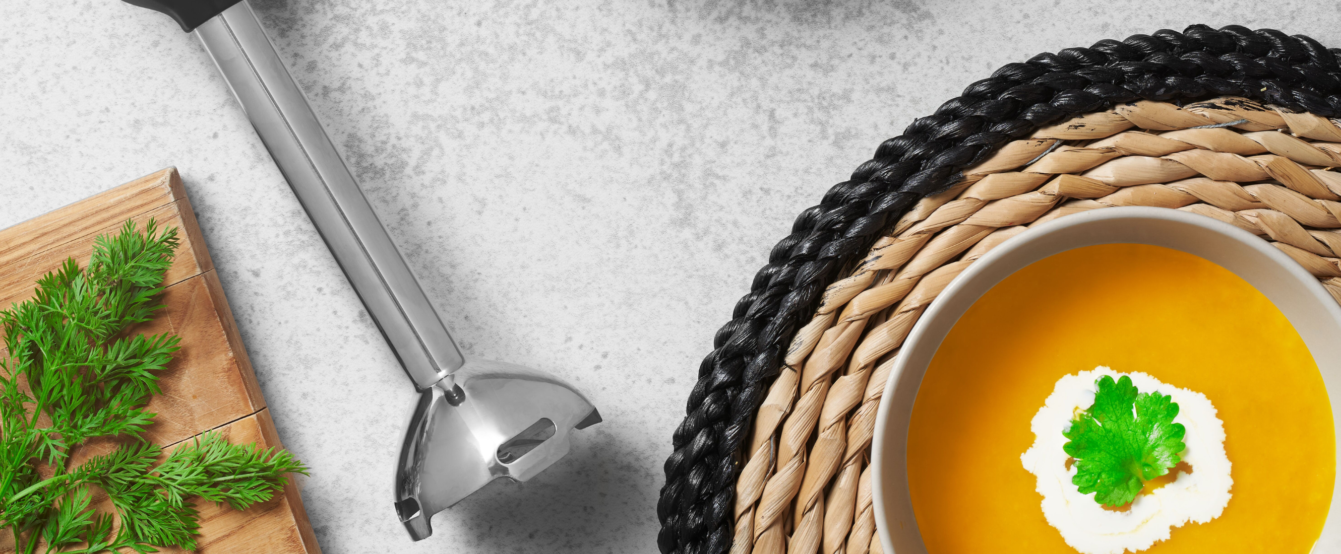Grey, Black-and-decker kitchen wand with immersion blender attachment lying next to a bowl of carrot, orange and ginger soup