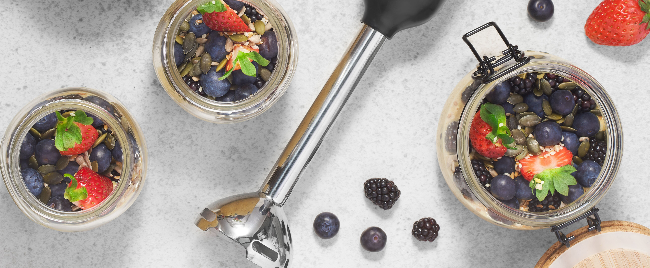 Grey, Black-and-decker kitchen wand with immersion blender attachment lying next to a jar of overnight oats, fruit and superfoods
